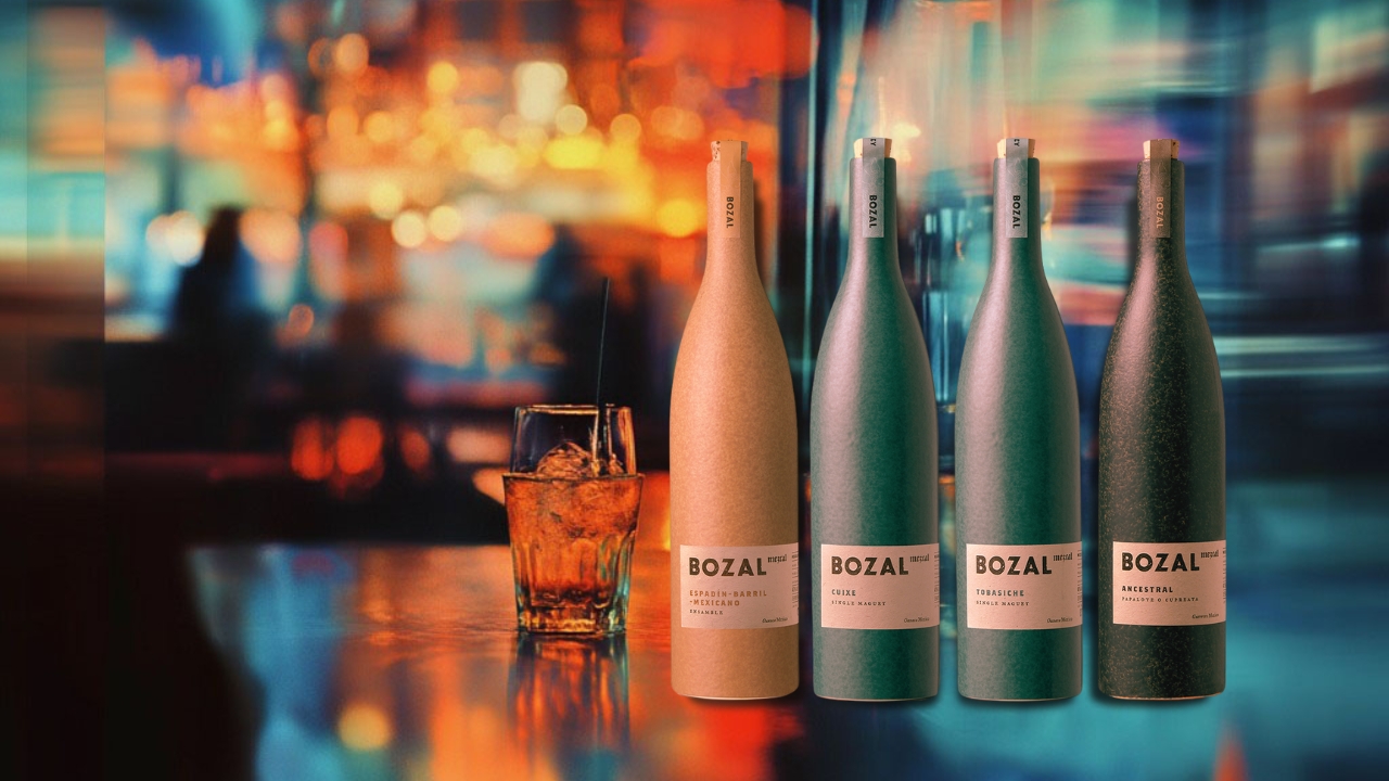 Collection of four Bozal Mezcal bottles displayed on a bar, with a blurred background featuring a cocktail glass and colorful lights, highlighting the vibrant atmosphere of a bar setting