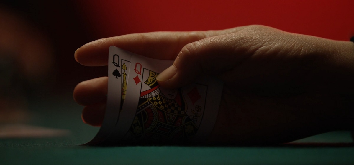 Hand holding a set of playing cards, featuring two queens, in a poker game setup