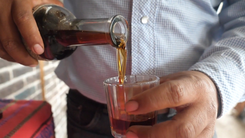 A Person Pouring Mezcal from A Bottle Into a Glass