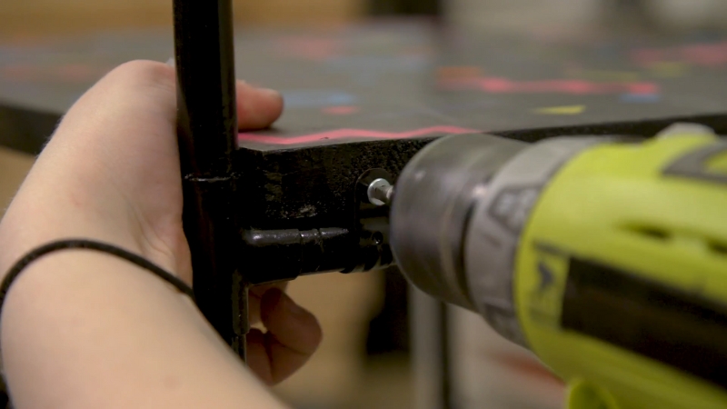 Close-up of a person using a power drill to secure the frame of a DIY bar cart with sturdy black wood and metal