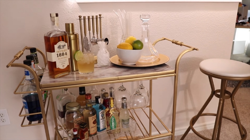 Gold-framed DIY bar cart with spirits, cocktail tools, and glassware neatly arranged on marble shelves