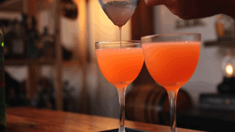 Two Division Bell cocktails being fine-strained into chilled coupe glasses