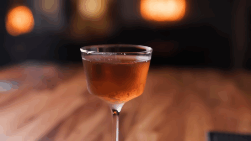 A Loaded Pistol cocktail served in a chilled coupe glass with a deep amber hue on a wooden bar