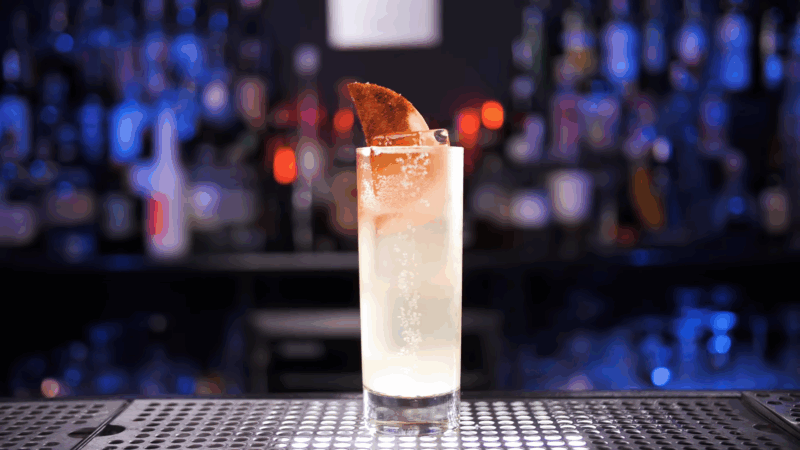 A tall Mezcal Paloma cocktail served over ice in a highball glass, garnished with a spiced grapefruit wedge