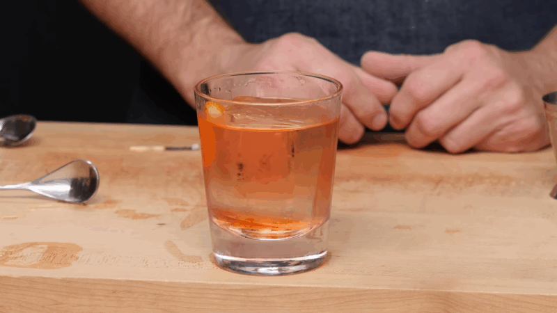 A chilled Oaxaca Old Fashioned cocktail with an orange peel garnish served in a rocks glass on a wooden bar counter