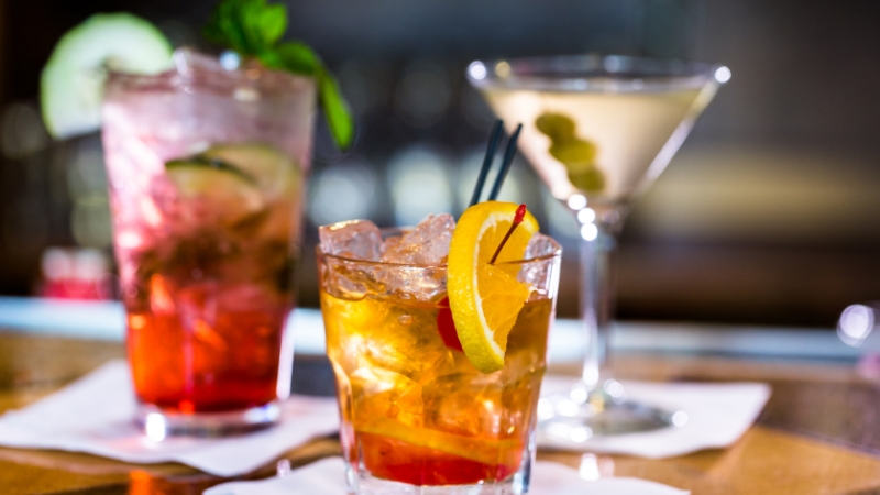 A lineup of colorful Mezcal cocktails on a bar, each garnished and served over ice or in classic glassware